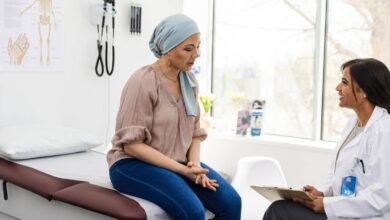 A-breast-cancer-patient-sits-on-the-examination-table-and-shares-her-symptoms-with-her-physician_GettyImages-2148188847-1536x1024